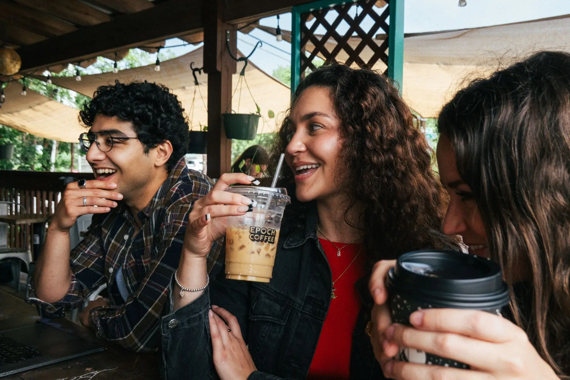 Friends laughing over iced coffee on the Epoch Coffee patio
