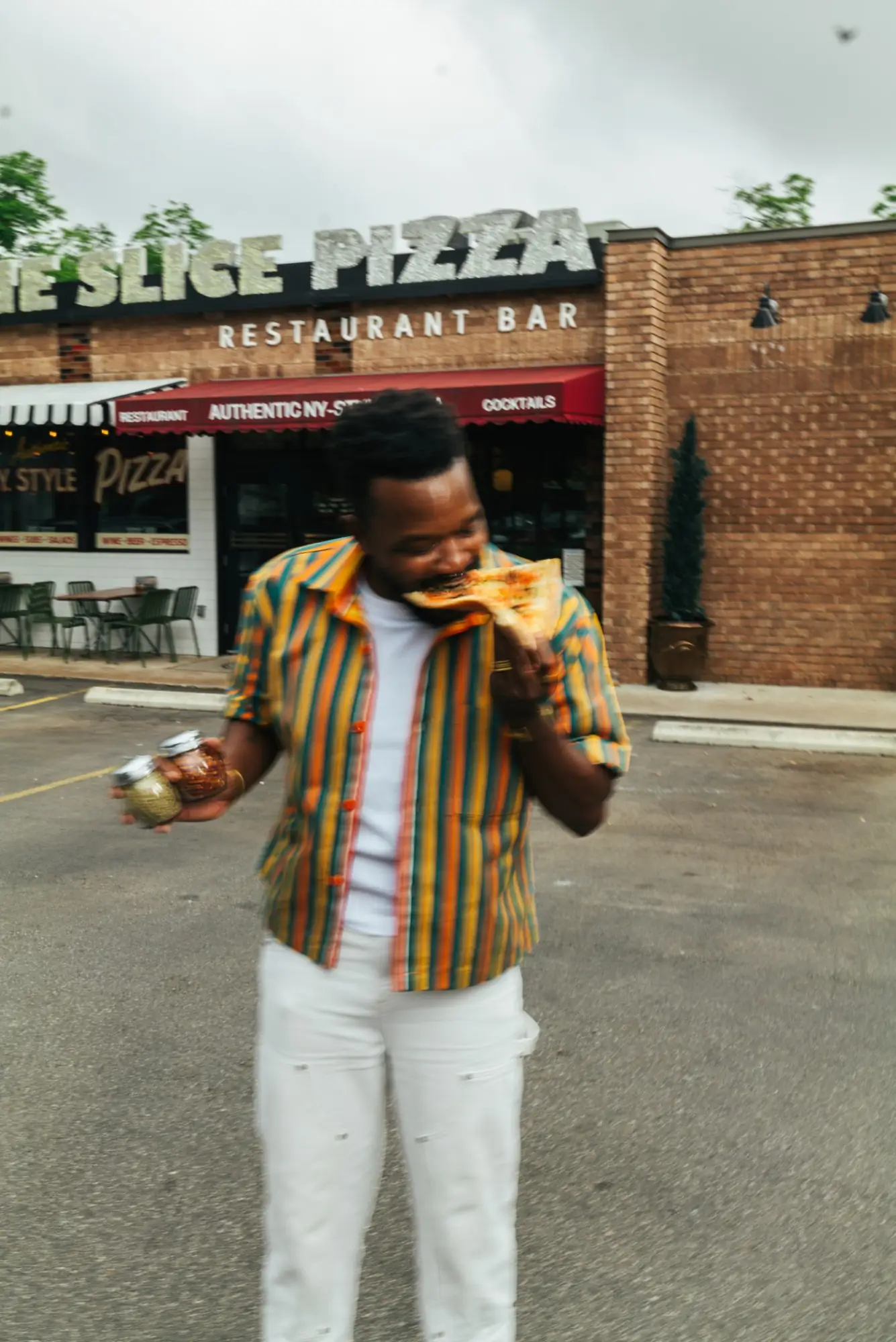 A man bites into a slice outside the neighborhood pizza restaurant